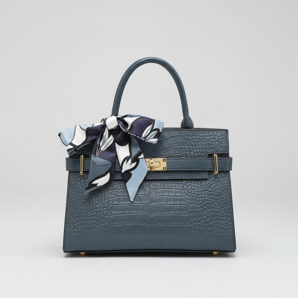 Person holding a dark blue handbag with a patterned scarf, wearing a white coat and black shoes.